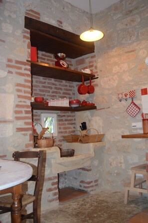 A rustic kitchen with exposed brick walls, wooden shelves, and hanging kitchen utensils.