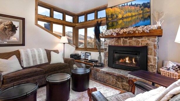 Un salon chaleureux avec une cheminée en pierre, une grande fenêtre donnant sur les montagnes, un canapé confortable et un téléviseur à écran plat fixé au-dessus de la cheminée.