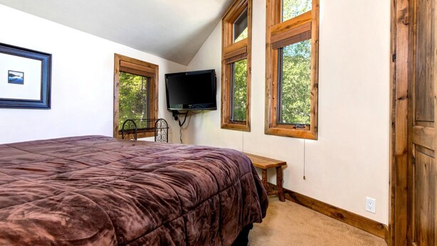 A bedroom with a large bed, a TV mounted on the wall, and a window with a view of trees. - Beautiful Air 3 Bedrooms POA-504B by KBM (Park City)