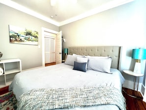 Un dormitorio con una cama grande, una mesita de noche, una lámpara, una puerta y un cuadro en la pared.