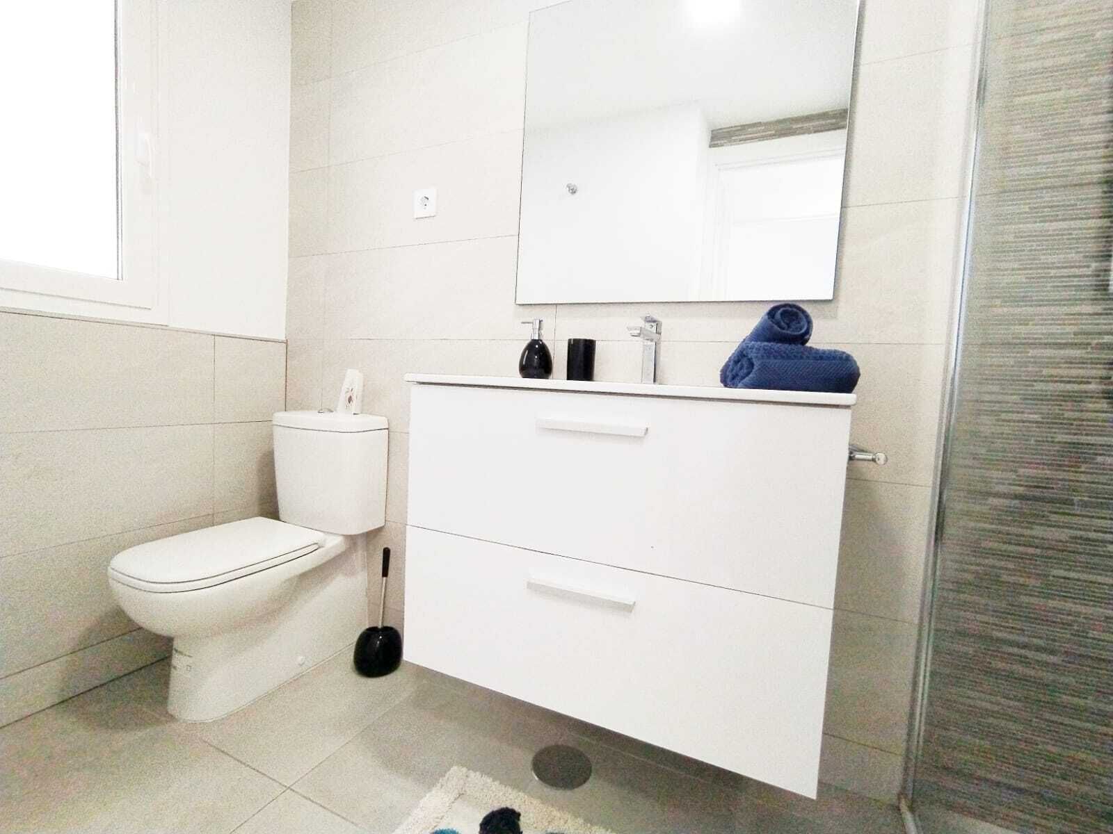 Ein modernes Badezimmer mit Toilette, einem weißen Waschtisch mit Spiegel und einem blauen Handtuch.