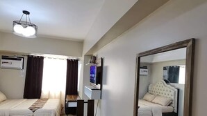 Ein Hotelzimmer mit zwei Betten, einem Esstisch mit Stühlen, einem Fernseher und einem großen Spiegel.