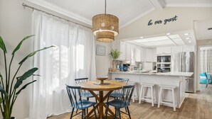 A modern kitchen with white cabinetry, a central island, and a dining area with a round table and chairs. - Cozy Family Beach Home, Golf Cart and near  StAndrews PCB (Panama City)
