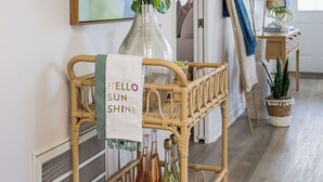 A wicker cart with a 'Hello Sun Shine' sign, a vase with green plants, and a bottle on a wooden floor. - Cozy Family Beach Home, Golf Cart and near  StAndrews PCB (Panama City)