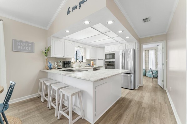A modern kitchen with white cabinetry, a central island with bar stools, stainless steel appliances, and a 'HAPPY PLACE' sign on the wall. - Family Resort Home with Golf cart, Heated Pool - Holiday Home (Panama City)