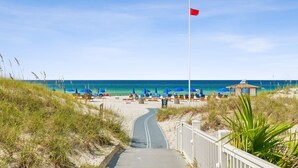 Ein Strand mit einem Weg zum Meer, blauen Sonnenschirmen und Liegestühlen.