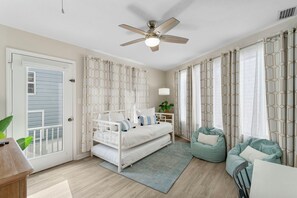 Ein Schlafzimmer mit einem weißen Bett, einem Deckenventilator, gemusterten Vorhängen und einem grünen Sitzsack.