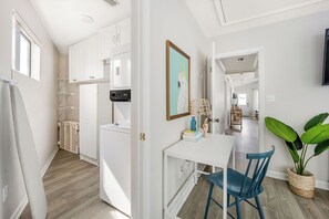 Eine moderne Küche mit weißen Schränken, einem eingebauten Backofen und einer Mikrowelle. Ein Essbereich mit einem weißen Tisch und blauen Stühlen sowie eine große Topfpflanze.