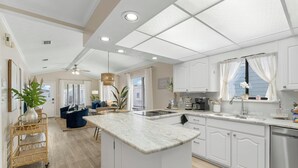 A spacious kitchen with white cabinetry, a central island, and a dining area with blue chairs. - Cozy Family Beach Home, Golf Cart and near  StAndrews PCB (Panama City)