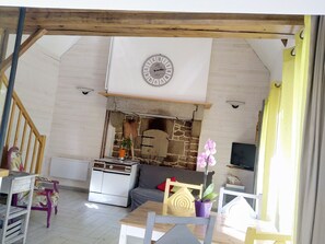 A rustic living room with a stone fireplace, a clock, and a dining area with a wooden table and chairs.