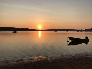 En stilla sjö vid solnedgången, med båtar och en strandlinje.