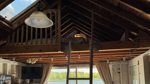 Een knus vakantiehuis met een slaapkamer op een entresol, een open haard, een televisie en uitzicht op een meer.