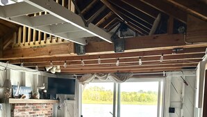 Een gezellige woonkamer met een schouw van baksteen, houten balken en een grote schuifdeur die leidt naar een terras.