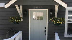 A house with a gray exterior, a white front door, and a number '303-1' above it. There are two flower planters on either side of the door. - Cozy first floor in-town condo. (Blowing Rock)
