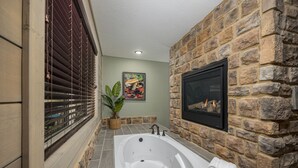 A bathroom with a stone wall, a large bathtub, a potted plant, and a framed picture on the wall. - Smoky Pines Chalet (Gatlinburg)
