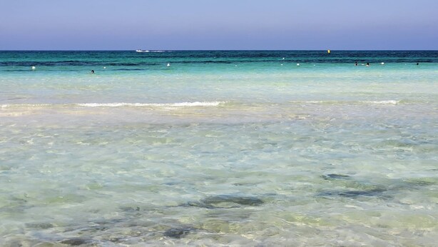 Una vista despejada de una playa con aguas tranquilas y un barco a lo lejos.