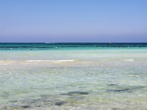 A clear view of a beach with calm waters and a distant boat.