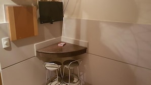 A small kitchen area with a countertop, two bar stools, a TV mounted on the wall, and a cabinet. - Hotel Namorata Expo Inn (São Paulo)