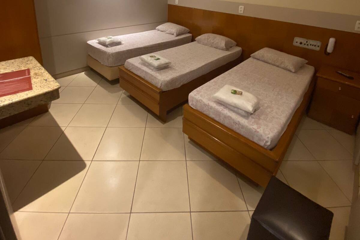 Una habitación pequeña y limpia con dos camas individuales, una mesita de noche de madera, una pequeña mesa y un cubo de basura negro.