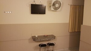 A bathroom with a TV mounted on the wall, a fan, a small countertop with a sink, and two bar stools. - Hotel Namorata Expo Inn (São Paulo)