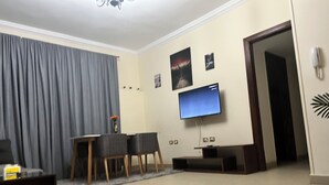 Ein Wohnzimmer mit flachbildfernseher an der Wand, einem Esstisch mit Stühlen, einem Sofa und einem Couchtisch.