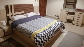 Ein Schlafzimmer mit einem Bett, Nachttischen, einer Kommode, einem Spiegel und einer Tür.
