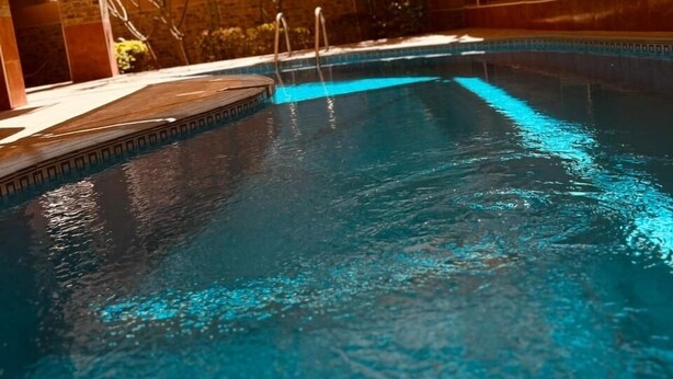 Ein Schwimmbecken mit klarem, blauem Wasser, umgeben von einer überdachten Fläche mit Fliesenboden und Holzwand.