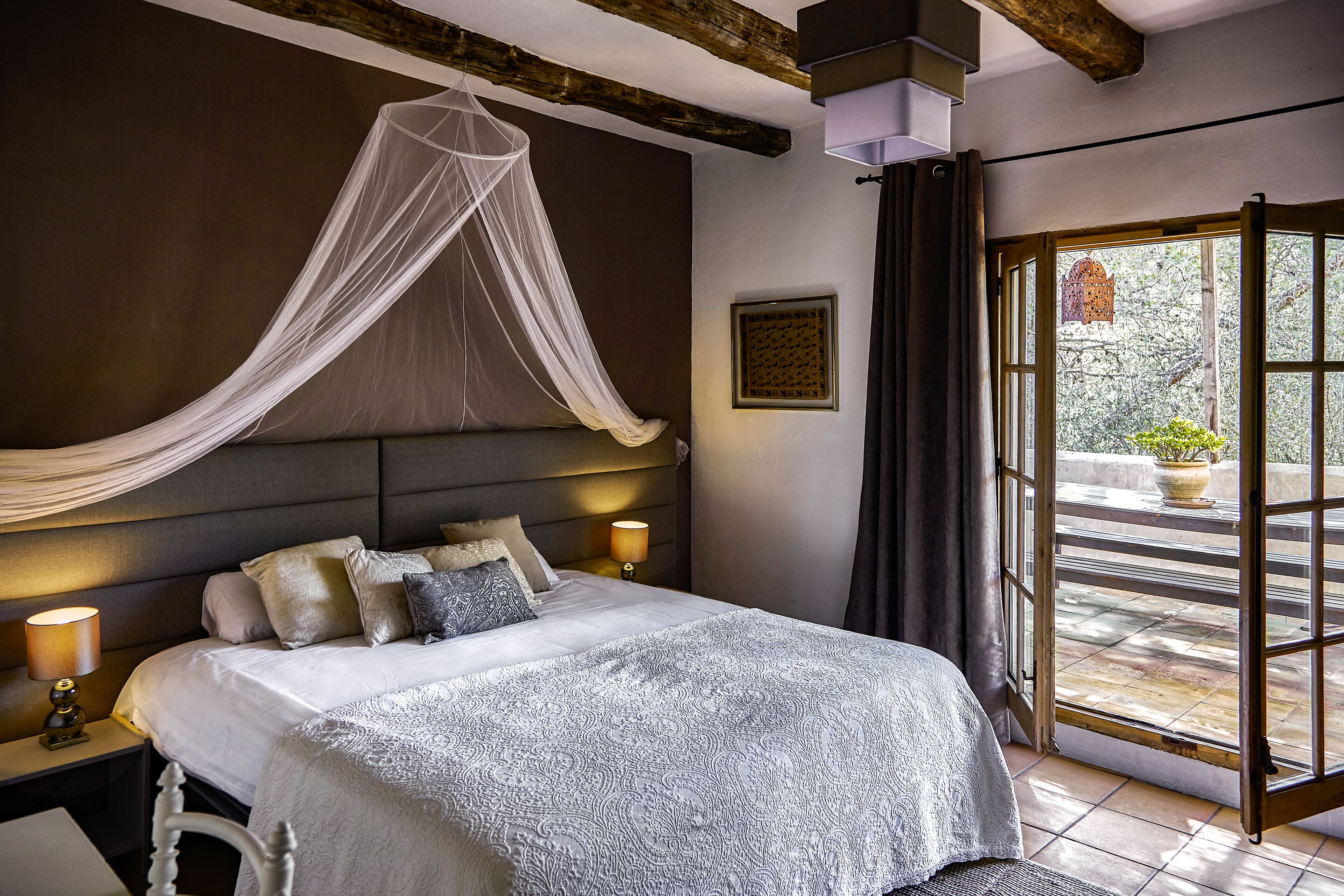 A bedroom with a bed, bedside lamps, a canopy, and a view of the outdoors.