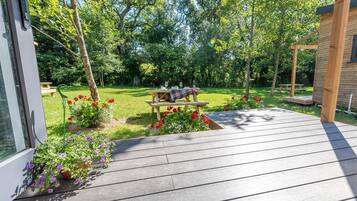 A wooden deck with a picnic table set up in a garden with a wooden fence and trees.