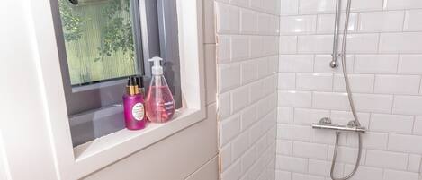 Un baño con lavabo blanco, ventana y zona de ducha.