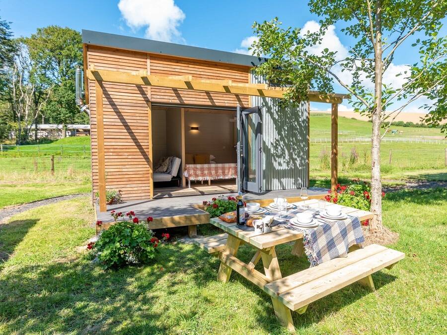 A wooden cabin with a covered outdoor seating area, a picnic table, and a small garden.