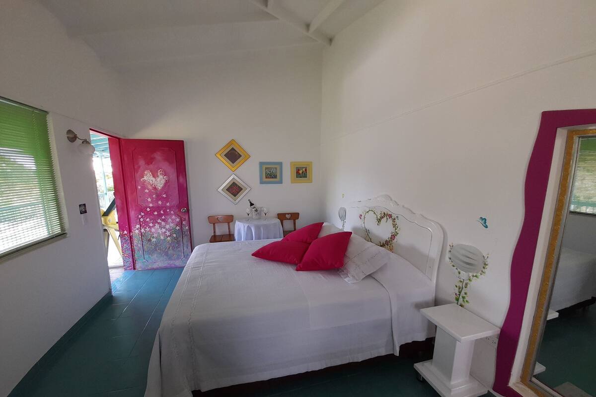 A bedroom with a bed, a bedside table, a mirror, and a door leading to another room.