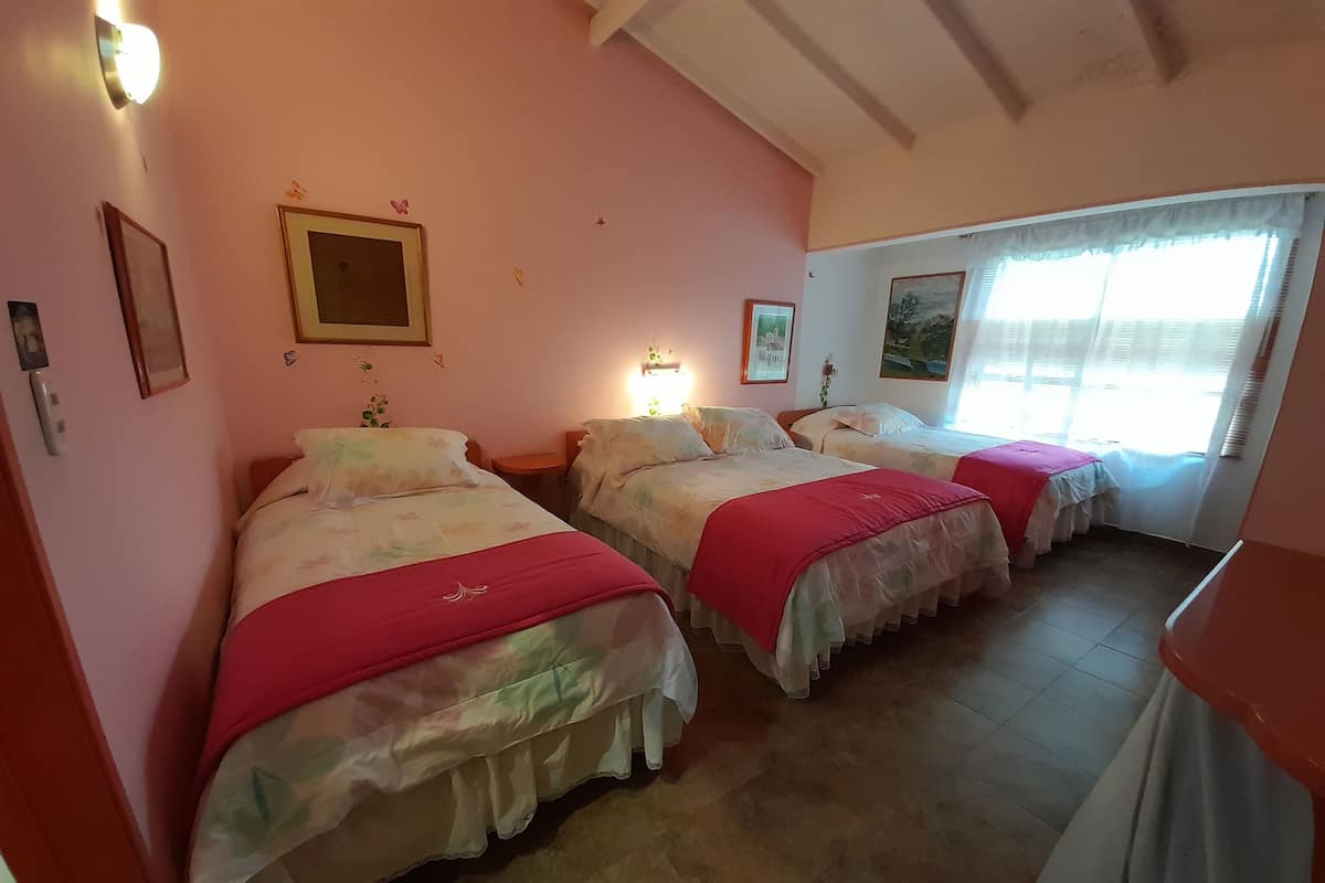 A hotel room with three beds, each with a red blanket, a wall-mounted light, and a framed picture.