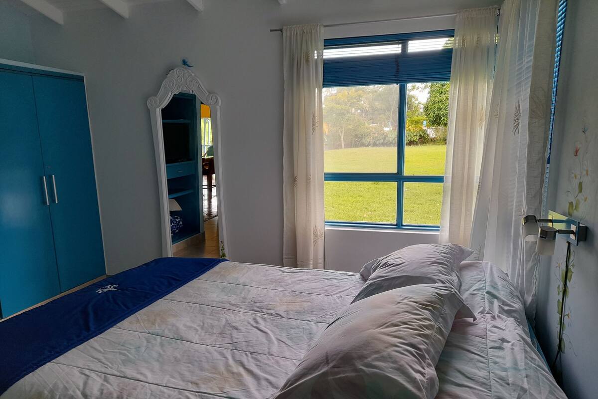 A bedroom with a bed, a wardrobe, a window with curtains, and a view of a green landscape.