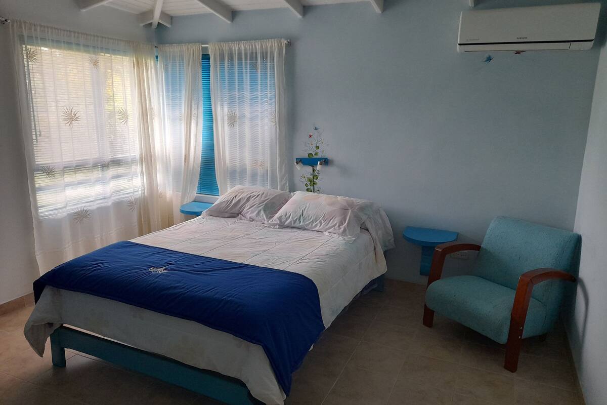 A bedroom with a bed, a chair, a small table, and a wall-mounted shelf.