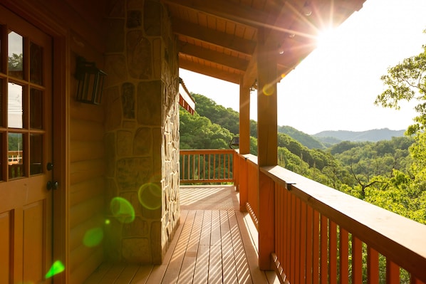 Une terrasse en bois, avec un muret en pierre et une balustrade en bois, donnant sur une vallée boisée.