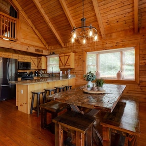 L’intérieur d’une cabane en bois, avec un grand îlot de cuisine, des tabourets de bar en bois et un lustre.