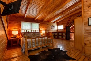Une chambre confortable dans un chalet en rondins, avec un lit en bois, un tapis en cuir et un téléviseur fixé au mur.