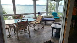 Una sala de estar con ventanales y vistas a un lago, amueblada con sillas y una mesa.