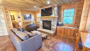 Un interior de cabaña acogedor con una chimenea de piedra, un sofá cómodo y un televisor montado encima.