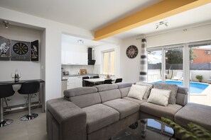 Relax in this stylish living space with a sofa, dining area, and kitchen, offering a view of the outdoor pool.