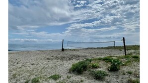 Een strandvolleybalnet op een zandstrand met uitzicht op de oceaan en een lichtbewolkte lucht.