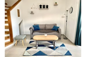 Een woonkamer met een grijze bank, blauwe kussens, een houten salontafel en een geometrisch vloerkleed.
