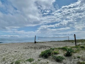 A beach volleyball net on a sandy beach with a view of the ocean and a partly cloudy sky.