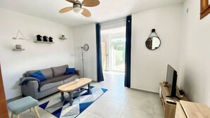 Een moderne woonkamer met een grijze bank, een houten salontafel, een klein krukje, een tv-meubel en een plafondventilator.