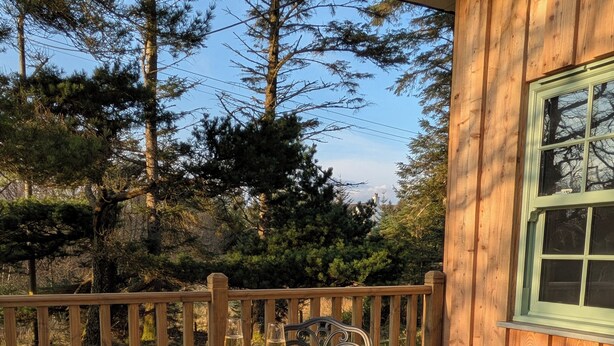 A wooden deck with a round table and two chairs, surrounded by a wooden fence and trees. - Tullochard House (Dunvegan)