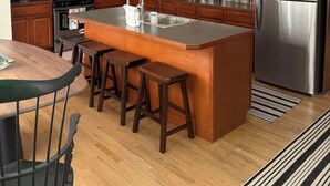 A modern kitchen with wooden cabinets, stainless steel appliances, a central island with stools, and a dining area with a table and chairs. - Perfect location in the heart of downtown Lenox (Lenox)