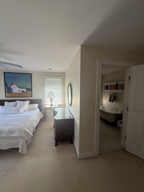 A bedroom with a bed, a desk, a chair, a lamp, a painting, and a bathroom visible through an open door. - Perfect location in the heart of downtown Lenox (Lenox)