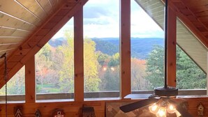 Interior de madera con ventanas amplias, un ventilador de techo y vistas a un paisaje boscoso.