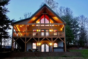 A two-story log cabin with a balcony on the upper floor, surrounded by trees. - Mountain Views / Golf / Hot Tub / Cozy Cabin! (Traphill)